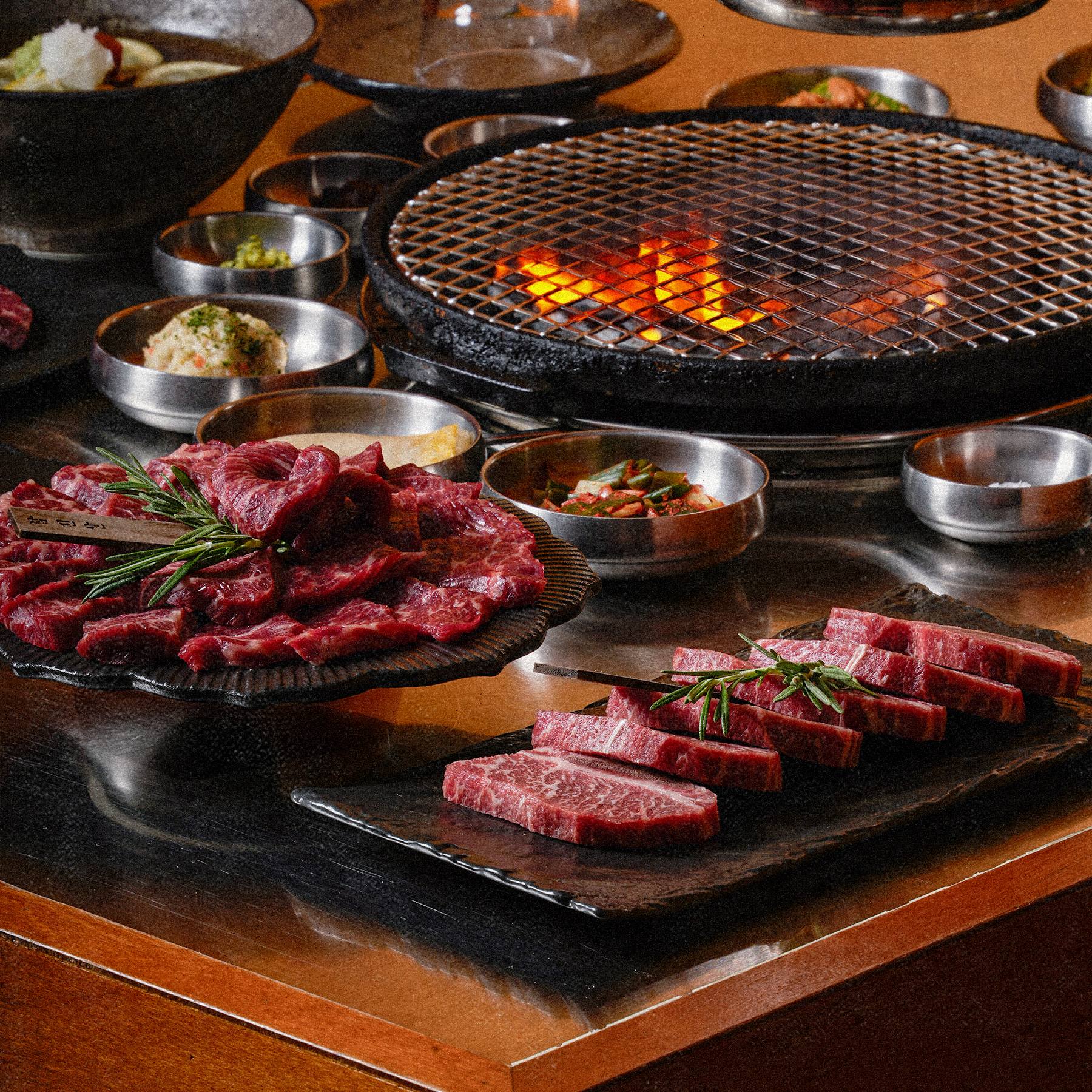 숯불이 타오르는 화로와 소고기, 반찬이 놓인 테이블